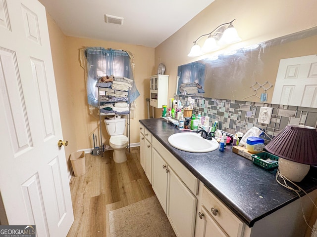 bathroom featuring wood-type flooring, toilet, vanity, and decorative backsplash