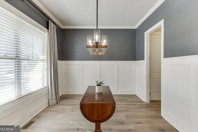 dining area featuring light wood finished floors, visible vents, an inviting chandelier, crown molding, and a decorative wall