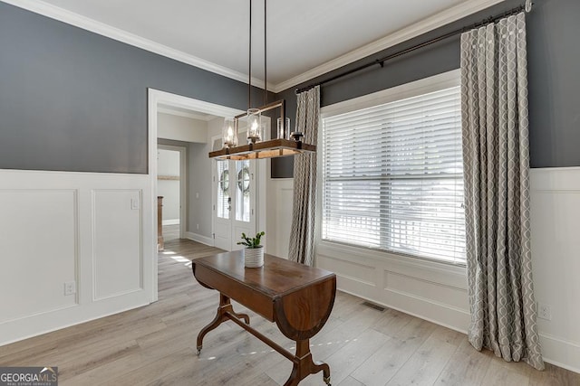 dining room featuring ornamental molding, light wood-type flooring, visible vents, and a decorative wall