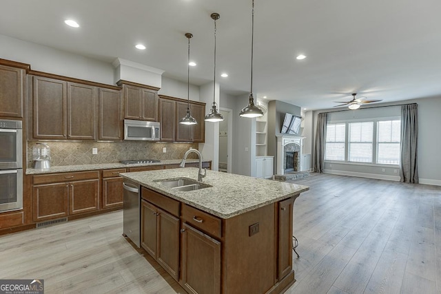 kitchen with stainless steel appliances, light wood-style floors, a fireplace with raised hearth, and a sink