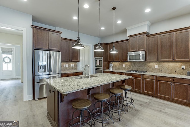 kitchen featuring a breakfast bar area, a kitchen island with sink, a sink, appliances with stainless steel finishes, and light stone countertops