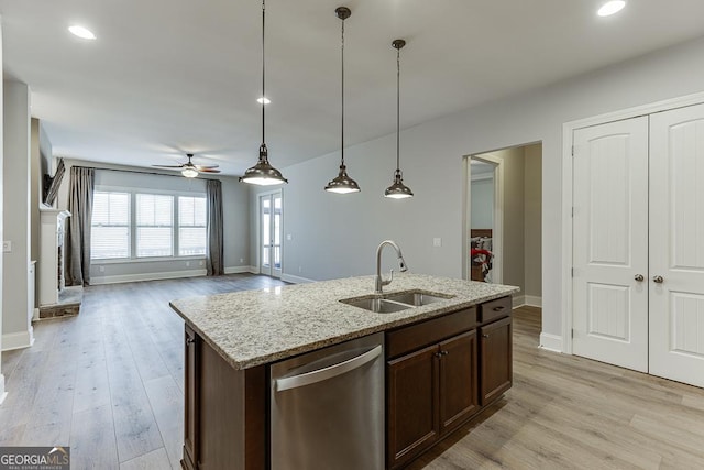 kitchen with light stone counters, stainless steel dishwasher, a kitchen island with sink, a sink, and light wood-type flooring