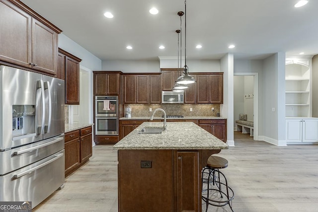 kitchen featuring light wood finished floors, stainless steel appliances, decorative backsplash, a kitchen island with sink, and a sink