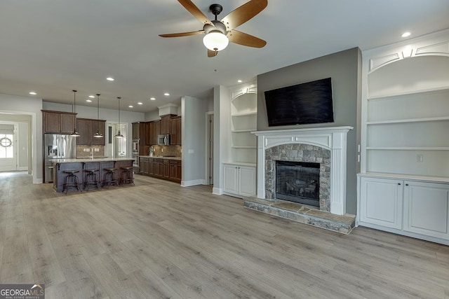 unfurnished living room featuring recessed lighting, a fireplace, a ceiling fan, built in features, and light wood finished floors