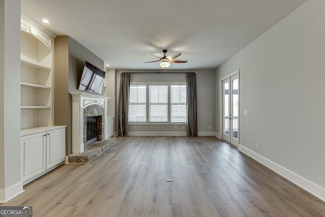 unfurnished living room with light wood finished floors, a stone fireplace, baseboards, and built in features