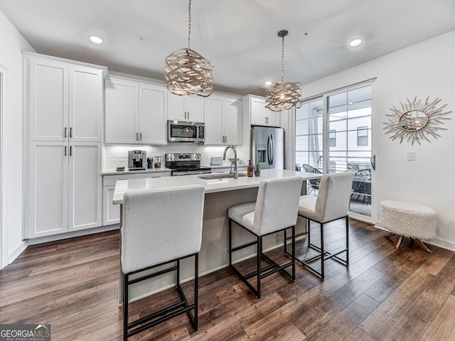 kitchen with sink, appliances with stainless steel finishes, a kitchen island with sink, hanging light fixtures, and white cabinetry