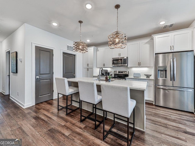 kitchen featuring appliances with stainless steel finishes, a kitchen island with sink, hanging light fixtures, white cabinetry, and dark hardwood / wood-style flooring