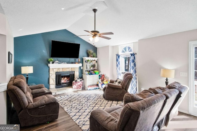 living room with a stone fireplace, wood-type flooring, lofted ceiling, ceiling fan, and a textured ceiling