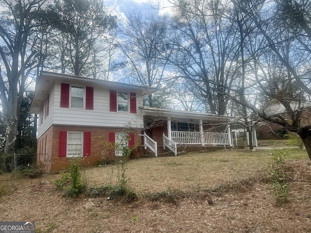 tri-level home featuring covered porch, brick siding, and fence