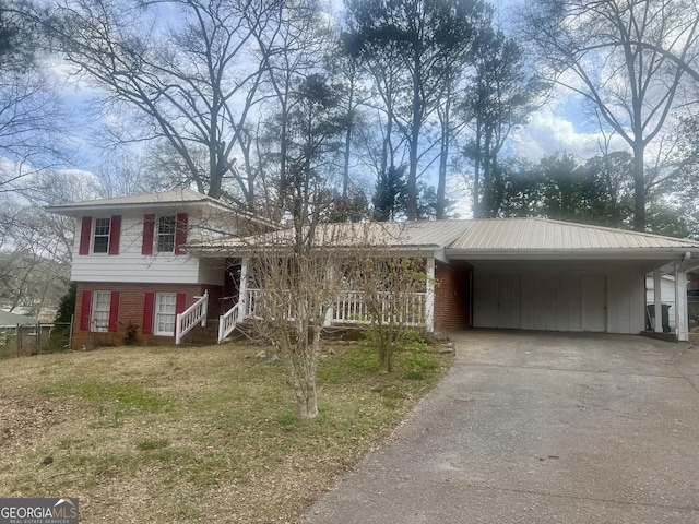 split level home featuring aphalt driveway, brick siding, fence, a carport, and a front lawn