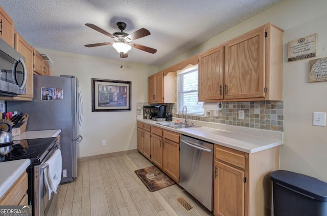 kitchen with sink, appliances with stainless steel finishes, a textured ceiling, decorative backsplash, and light wood-type flooring