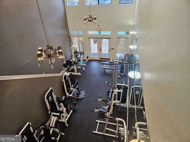 gym featuring a notable chandelier, a towering ceiling, and french doors