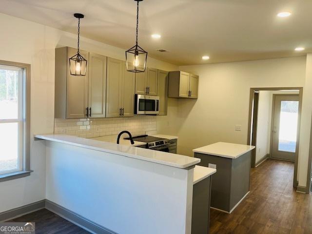 kitchen featuring pendant lighting, decorative backsplash, kitchen peninsula, stainless steel appliances, and dark wood-type flooring