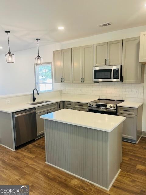 kitchen with gray cabinets, pendant lighting, sink, stainless steel appliances, and dark wood-type flooring