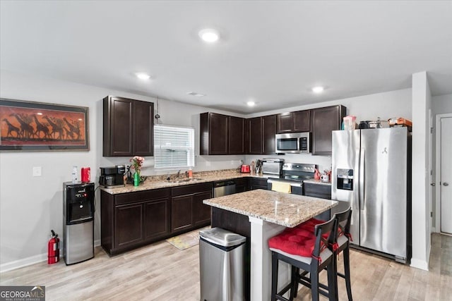 kitchen with a breakfast bar area, light wood-style flooring, stainless steel appliances, a sink, and a center island