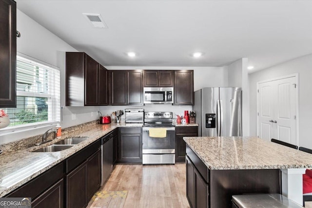 kitchen with dark brown cabinetry, stainless steel appliances, a sink, visible vents, and light wood-type flooring