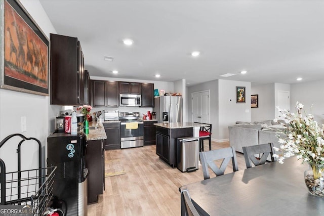 kitchen with light wood-style flooring, stainless steel appliances, a center island, open floor plan, and light stone countertops