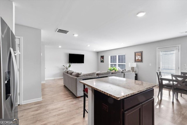 kitchen featuring visible vents, stainless steel fridge with ice dispenser, a kitchen island, open floor plan, and light wood-type flooring