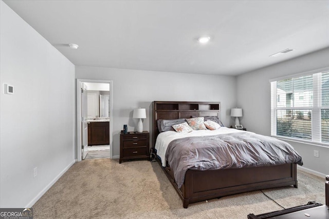 bedroom with baseboards, ensuite bath, visible vents, and light colored carpet