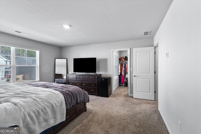 bedroom featuring light carpet, baseboards, visible vents, and a walk in closet