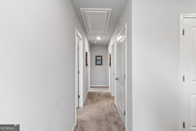 corridor featuring baseboards, attic access, and light colored carpet