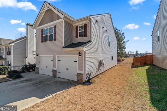 view of side of home featuring a yard, concrete driveway, fence, a garage, and stone siding