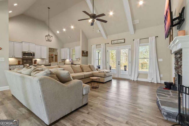 living room featuring ceiling fan, high vaulted ceiling, a fireplace, french doors, and light wood-type flooring