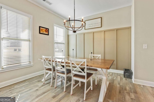 dining area with a notable chandelier, ornamental molding, and light wood-type flooring