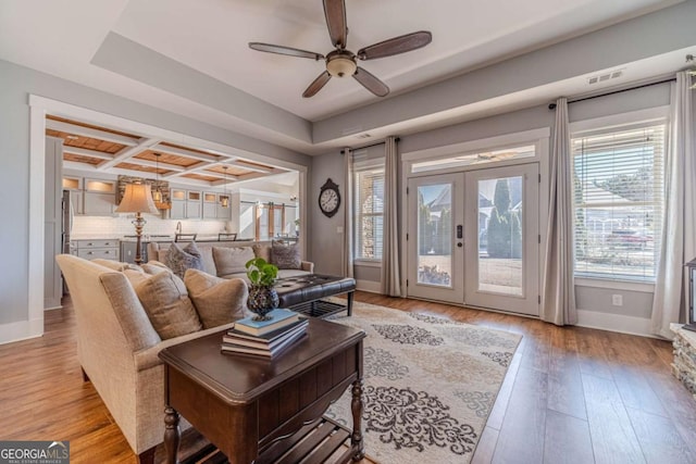 living room with beamed ceiling, coffered ceiling, ceiling fan, light wood-type flooring, and french doors