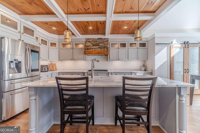 kitchen featuring stainless steel refrigerator with ice dispenser, a large island, decorative light fixtures, and light stone counters