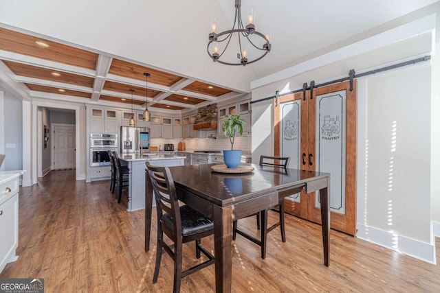 dining room with coffered ceiling, a chandelier, beamed ceiling, a barn door, and light hardwood / wood-style floors