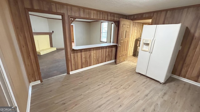 kitchen featuring white refrigerator with ice dispenser, wood walls, a textured ceiling, and light wood-type flooring