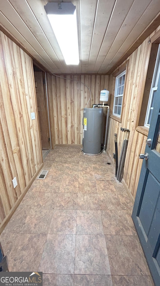 basement with wooden ceiling, water heater, and wood walls