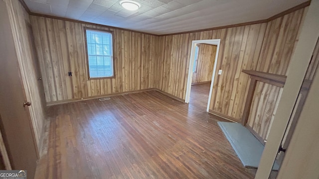 empty room with crown molding, dark wood-type flooring, and wooden walls