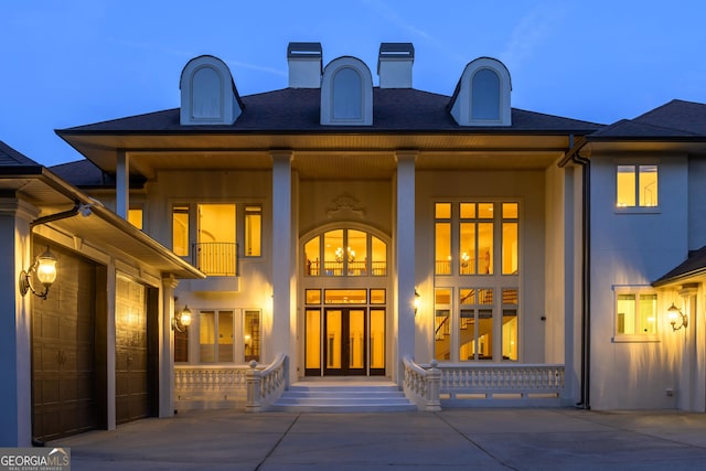 back house at dusk with a garage, a balcony, and covered porch