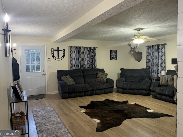 living room featuring ceiling fan, wood-type flooring, beam ceiling, and a textured ceiling