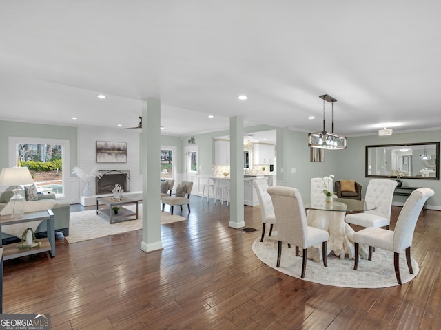 dining space with crown molding, plenty of natural light, dark hardwood / wood-style floors, and a brick fireplace