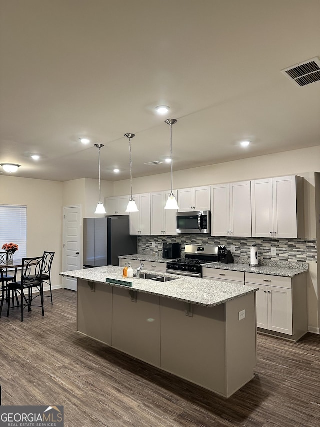 kitchen featuring decorative light fixtures, white cabinets, stainless steel appliances, light stone countertops, and a center island with sink