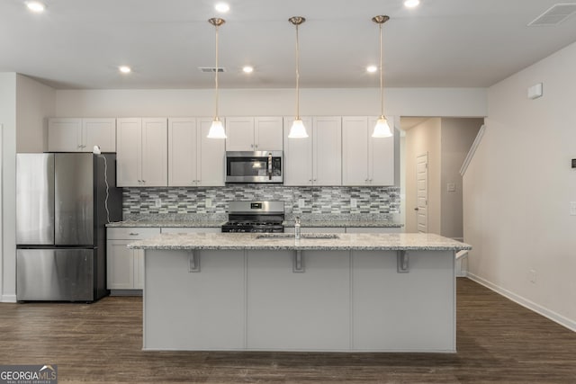 kitchen with a kitchen island with sink, light stone countertops, stainless steel appliances, and white cabinets