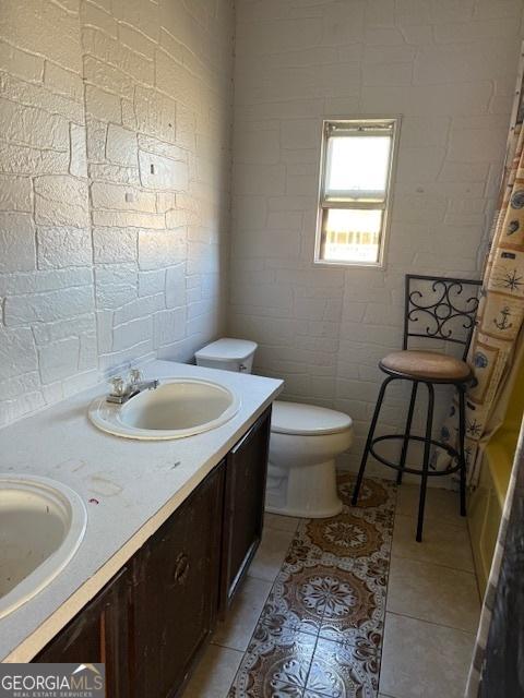 bathroom featuring brick wall, toilet, tile patterned flooring, and vanity