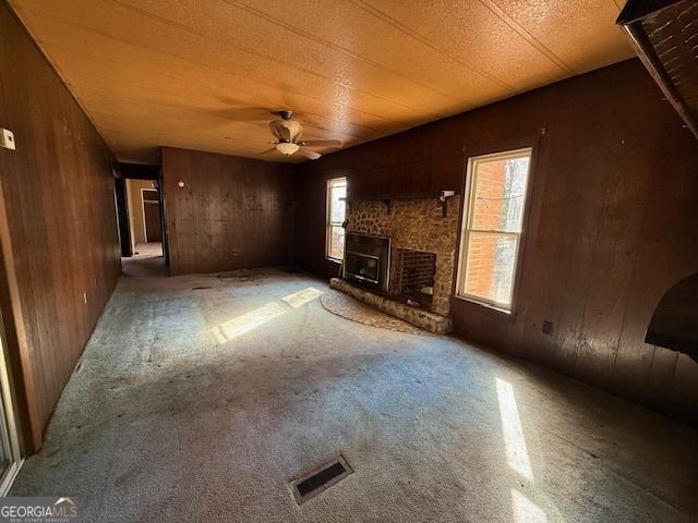 unfurnished living room featuring a brick fireplace, ceiling fan, a healthy amount of sunlight, and wood walls