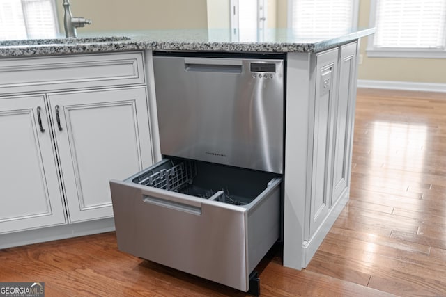 kitchen with sink, dishwasher, light stone counters, white cabinets, and light wood-type flooring