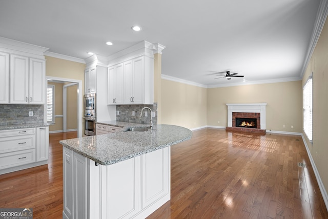 kitchen with light stone counters, sink, white cabinets, and a brick fireplace