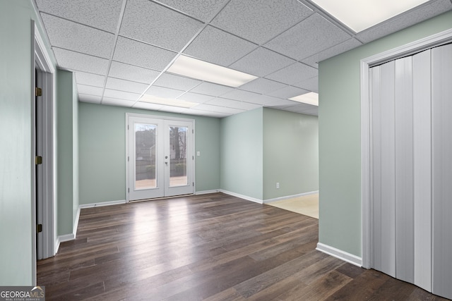 spare room with a drop ceiling, dark wood-type flooring, and french doors