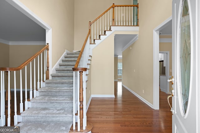 stairs featuring hardwood / wood-style floors, ornamental molding, and a high ceiling