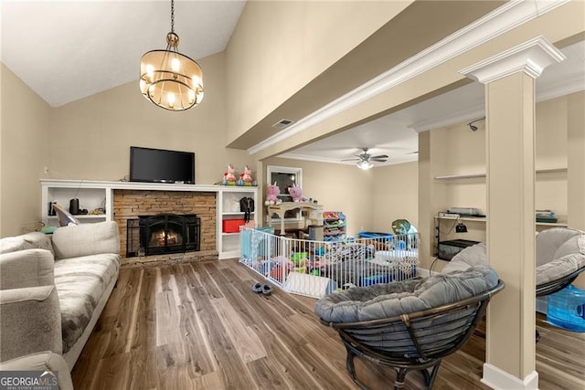 living room with lofted ceiling, a stone fireplace, hardwood / wood-style floors, crown molding, and ceiling fan with notable chandelier