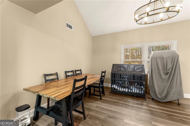 dining space with hardwood / wood-style flooring, a chandelier, and vaulted ceiling