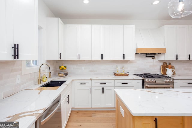 kitchen with white cabinetry, premium range hood, appliances with stainless steel finishes, and light stone counters