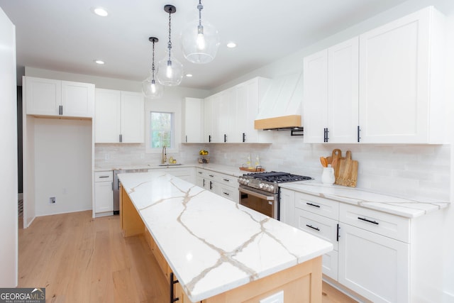 kitchen featuring stainless steel gas range, hanging light fixtures, custom range hood, white cabinets, and a kitchen island