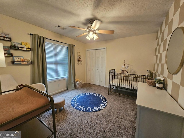 bedroom with dark colored carpet, a textured ceiling, a closet, a nursery area, and ceiling fan